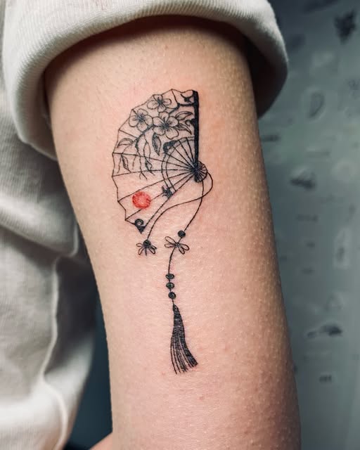 Tatuaje fine-line de abanico floral con detalle en color y borla